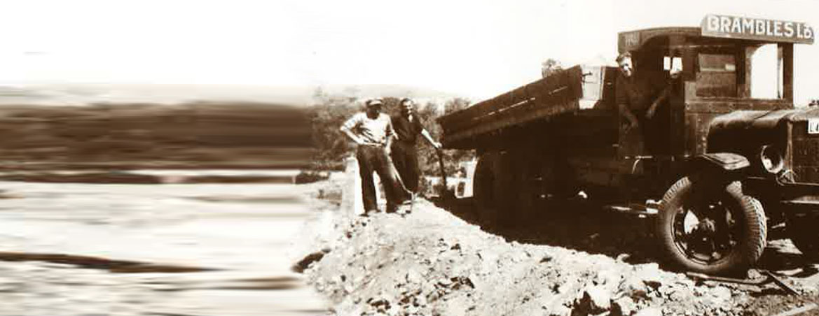 A sepia-toned historical image of two men with shovels standing by an old Brambles truck unloading materials