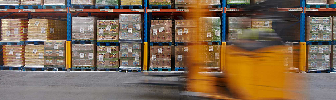 A photograph of a moving forklift in a warehouse in front of pallets of stock