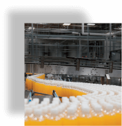 An image of hundreds of drinking bottles filled with orange liquid travelling on a conveyor belt in a warehouse environment